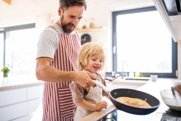 child and dad making pancake together