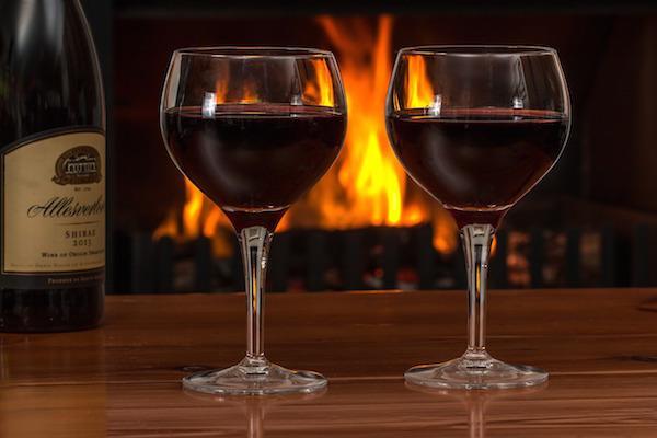 red wine in two glasses in front of a roaring fire