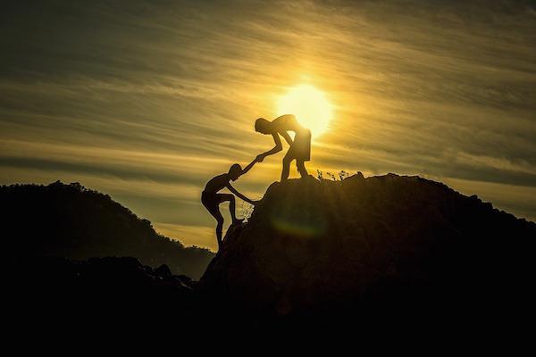 person helping another person up a rocky hill